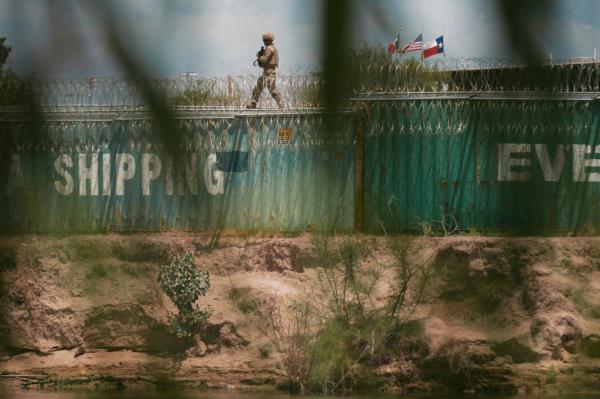A member of the Texas Army National Guard patrols the Rio Grande from atop a line of shipping containers in Eagle Pass, Texas.