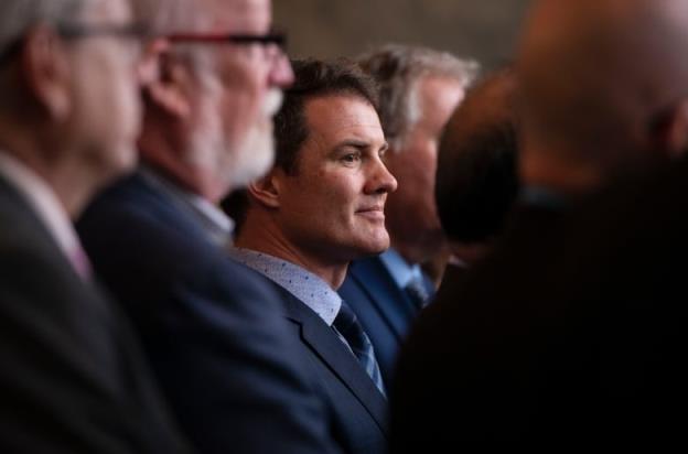 A side shot of a man standing among other people in a suit.